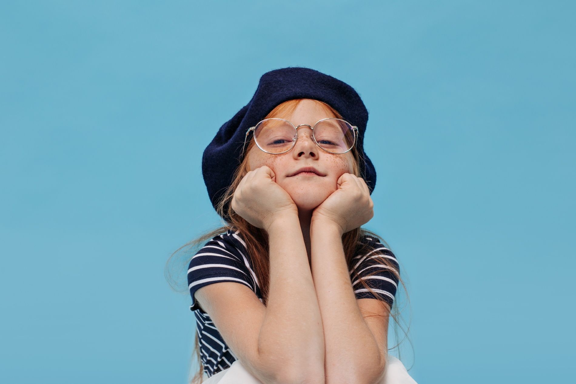 clever-little-girl-with-freckles-stylish-hat-clear-glasses-posing-looking-front-blue-isolated-wall-1
